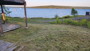 A wooden deck with a grassy area in front, overlooking a lake with a boat in the distance. - Oceanside beautiful vacation property! (Lewisporte)
