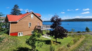 A wooden house with a red roof, a deck, and a view of a lake. - Oceanside beautiful vacation property! (Lewisporte)