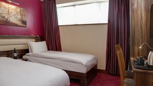 Habitación de hotel con dos camas, cabecero de madera, escritorio con silla, ventana con cortinas y un cuadro en la pared.