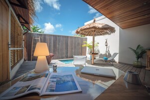 Une terrasse en bois avec un parasol en chaume, un ordinateur portable, un livre et une petite table avec une lampe.