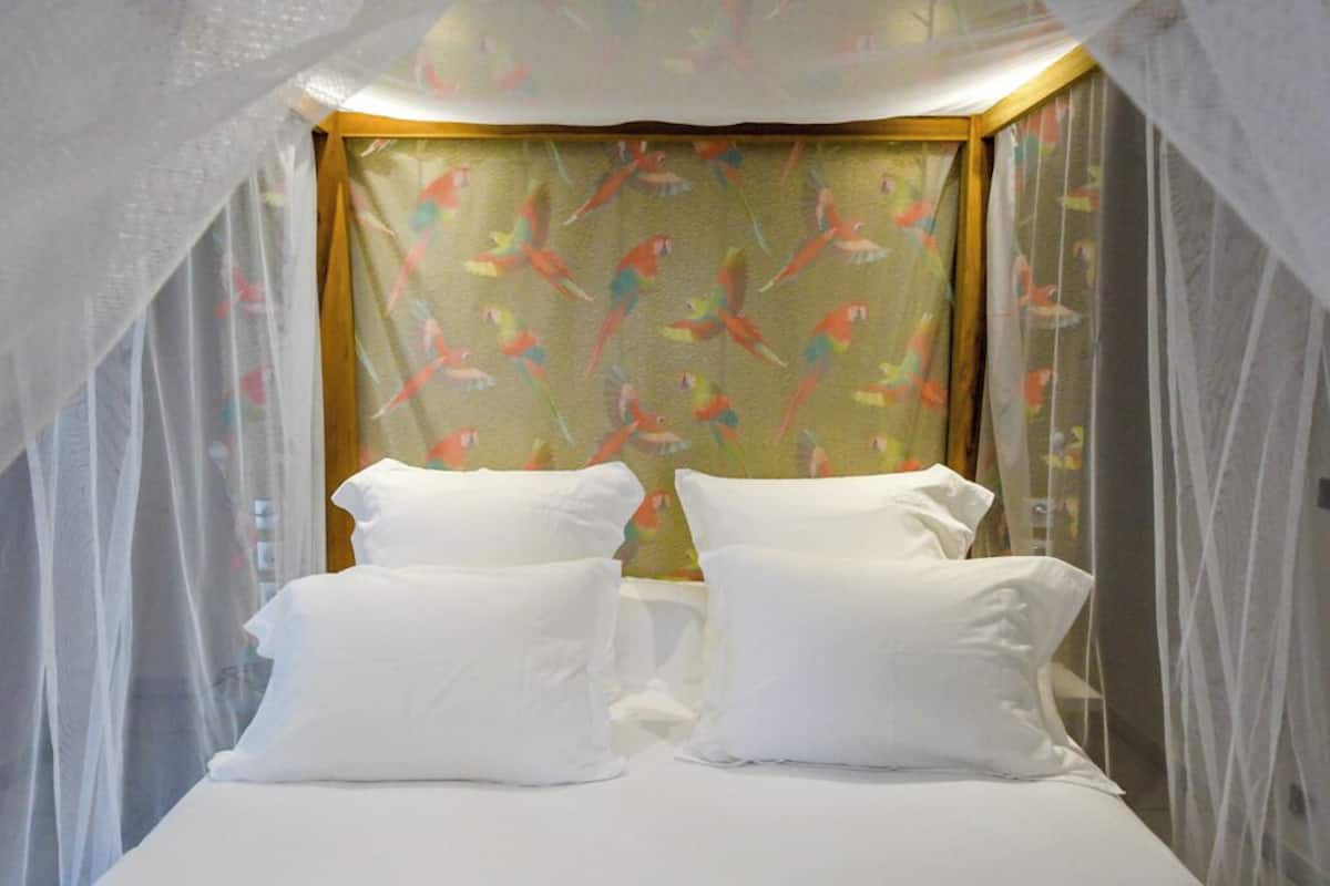 A bed with white pillows and a mosquito net overhead.