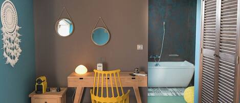 Une pièce avec un bureau en bois, une chaise jaune, une table de chevet et un miroir fixé au mur.