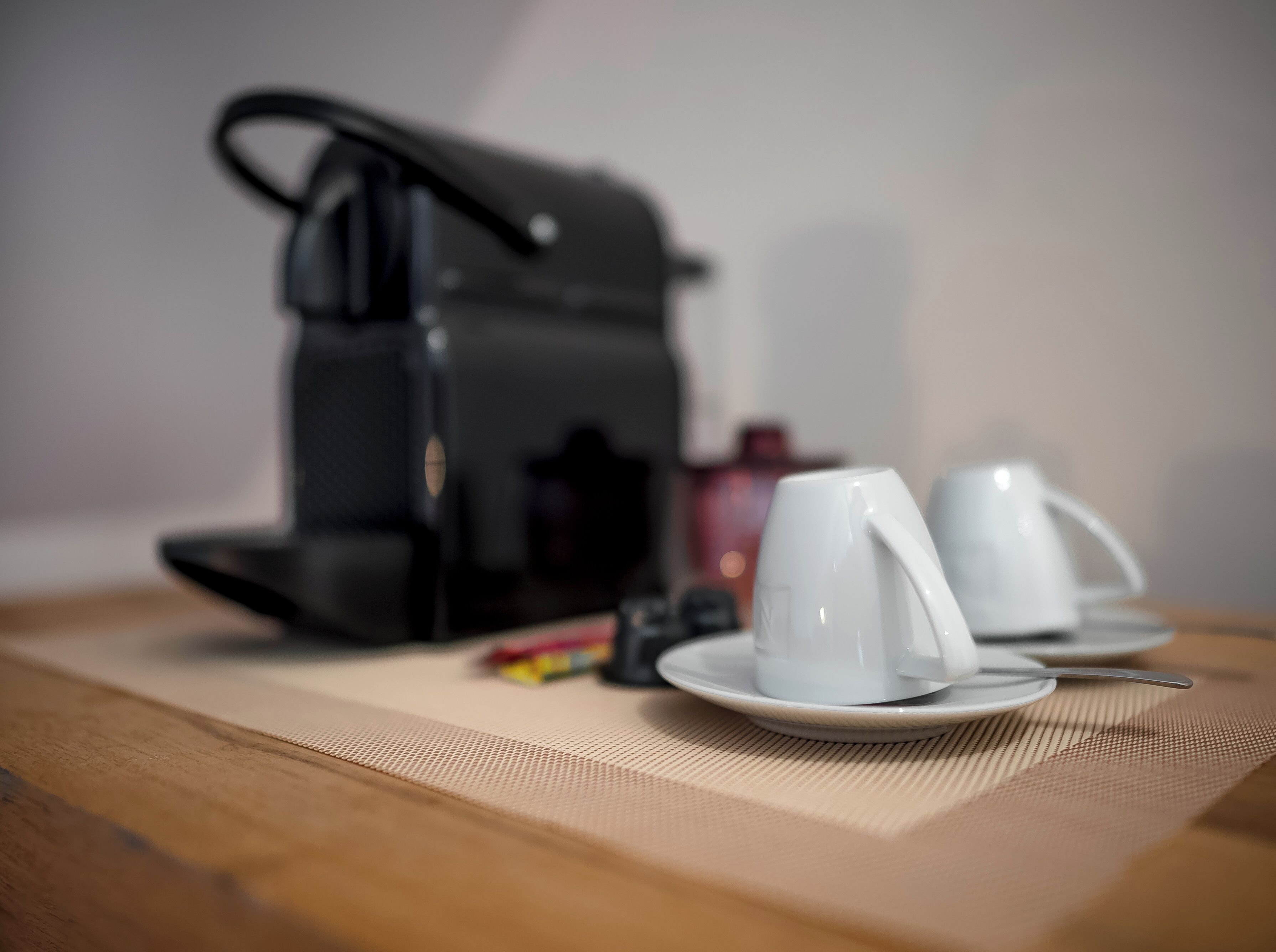 A coffee maker on a table with two white cups and a saucer.