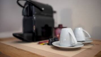 A coffee maker on a table with two white cups and a saucer.