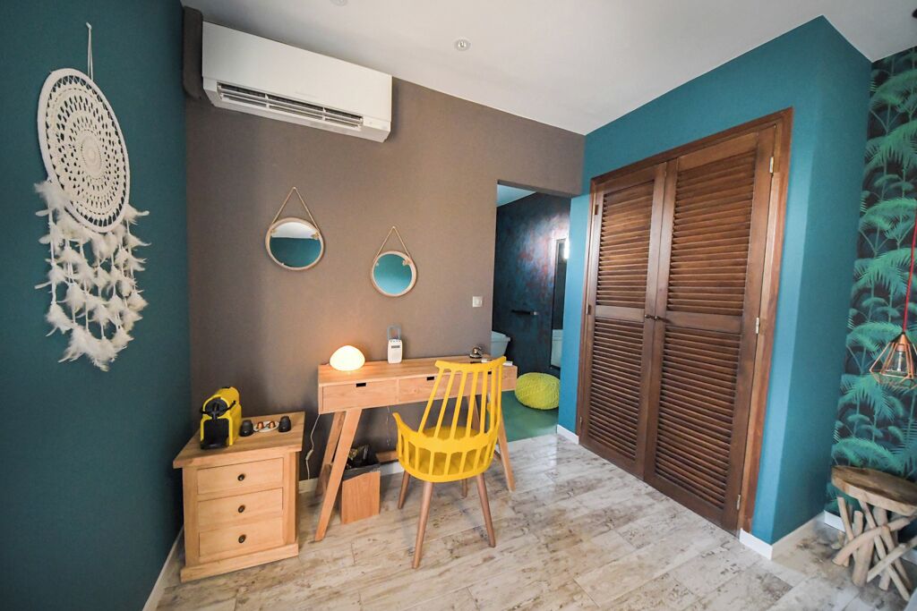 Una stanza dalle pareti color acquamarina, una scrivania in legno con una sedia, un piccolo armadietto in legno e un'ampia porta in legno con pannelli a persiana.