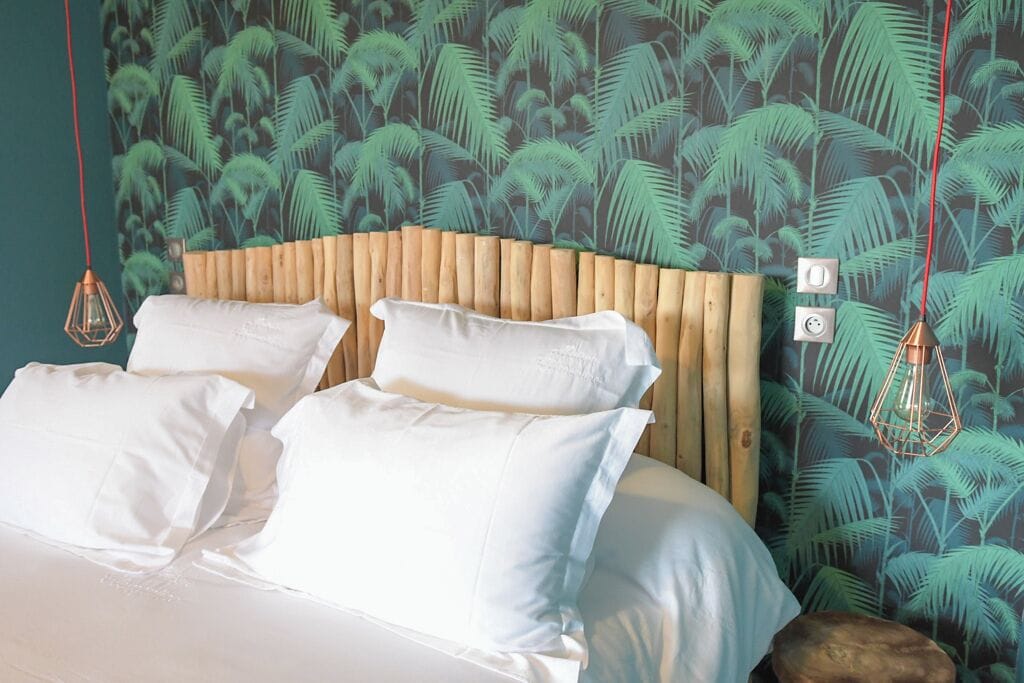 A bed with white linens, a wooden headboard, and a tropical leaf-patterned wall.
