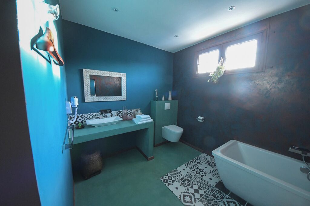 A bathroom with a bathtub, a sink with a mirror, a toilet, and a window with a plant.