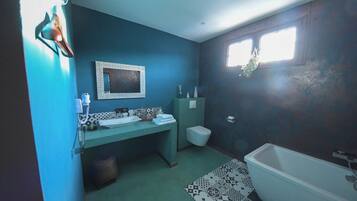 A bathroom with a bathtub, a sink with a mirror, a toilet, and a window with a plant.
