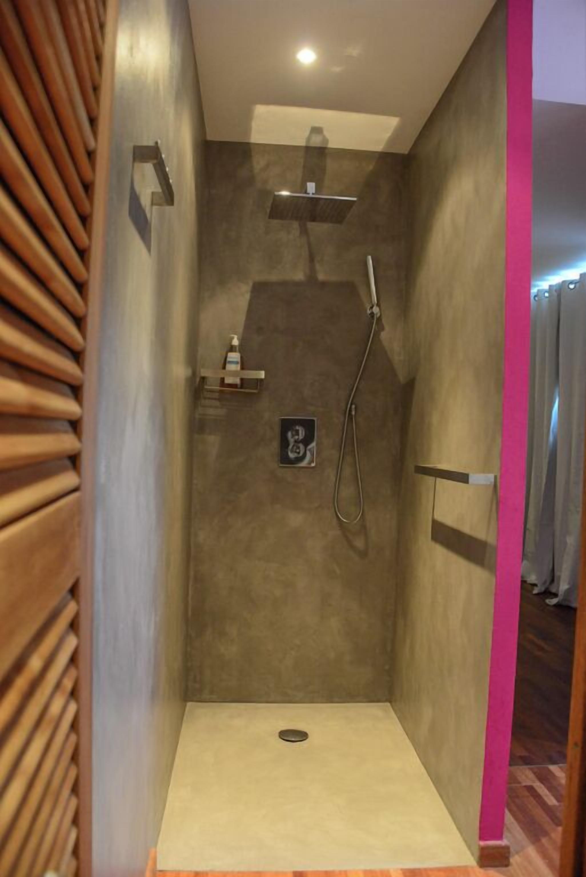 Een moderne douche met een handdouche, een zeepdispenser en een klein plankje.