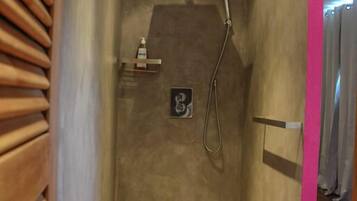 Een moderne douche met een handdouche, een zeepdispenser en een klein plankje.