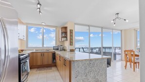 Une cuisine moderne dotée d’un grand îlot central, de meubles en bois, d’appareils électroménagers en acier inoxydable et offrant une vue sur l’extérieur.