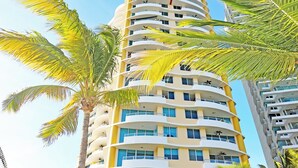 Un grand hôtel à plusieurs étages, doté d’une façade incurvée, entouré de palmiers et d’un jardin bien entretenu.