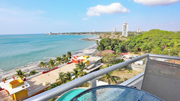 Un balcon avec piscine, offrant une vue sur une plage et le paysage urbain.