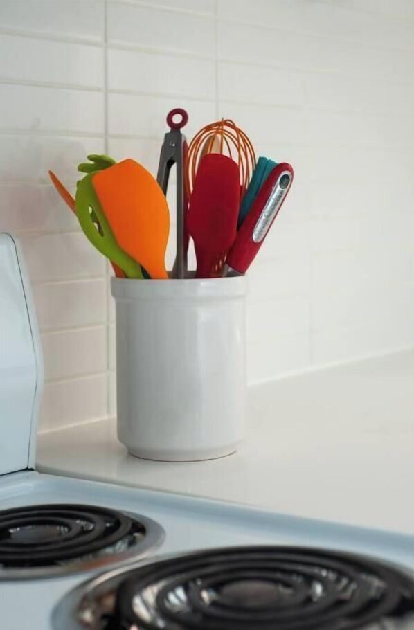 A white kitchen with a white stove and a utensil holder containing various kitchen tools.