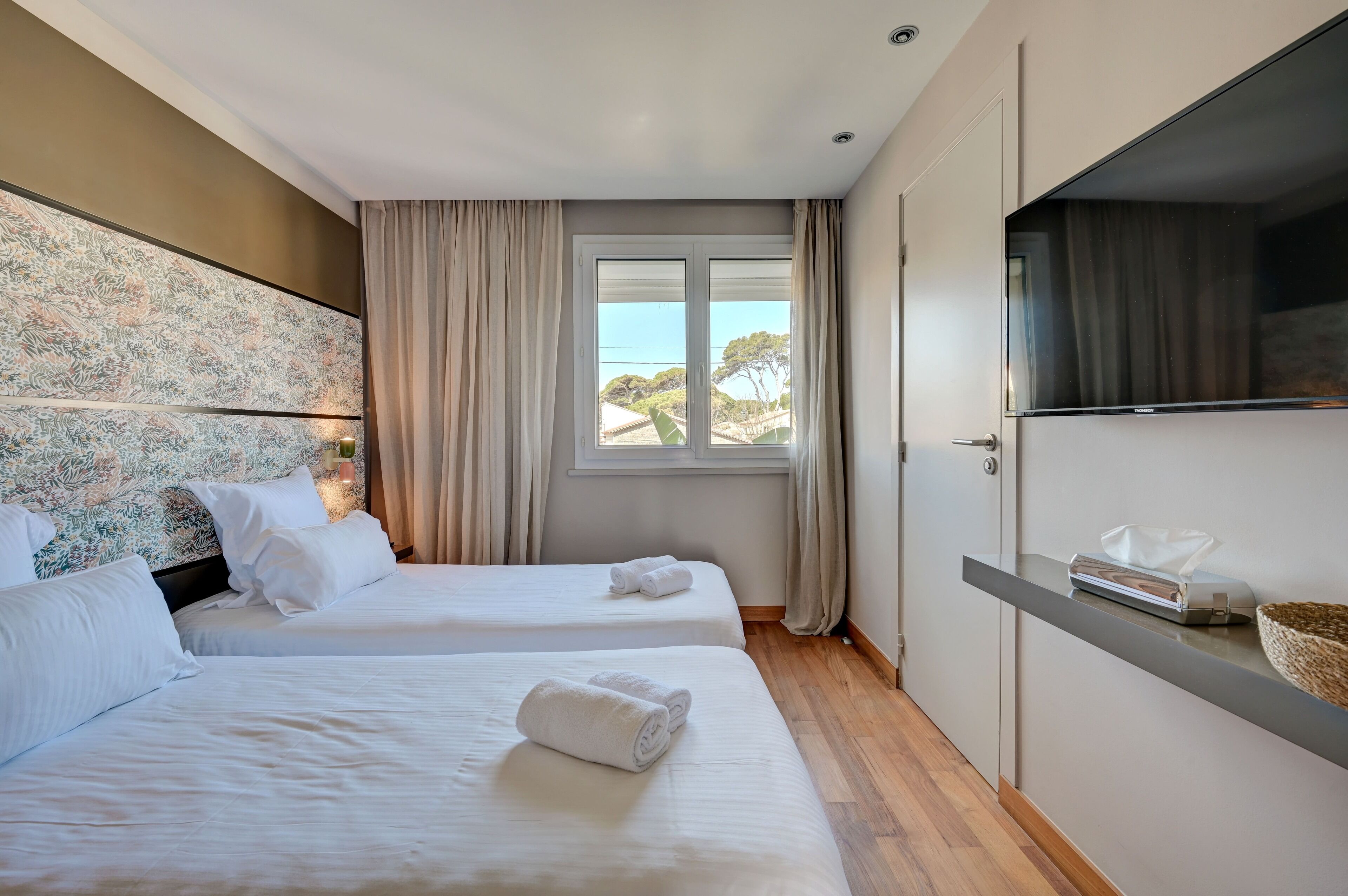 Une chambre d’hôtel avec deux lits, une grande fenêtre avec des rideaux, un téléviseur à écran plat et un mini-bar.