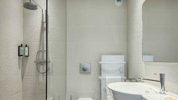 Un baño moderno con ducha de vidrio, inodoro blanco y tocador con un espejo grande.