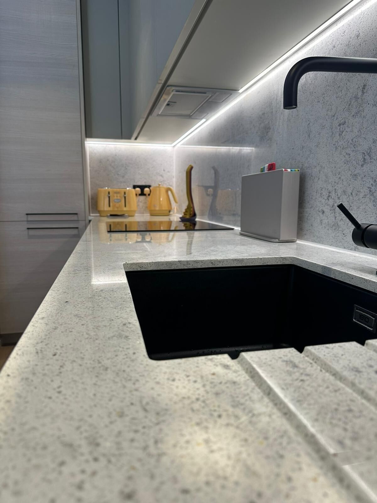 A modern kitchen with a built-in black sink, stainless steel cabinets, and a marble countertop.