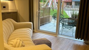 Ein modernes Wohnzimmer mit einer Couch, einem kleinen Tisch und Blick auf einen Balkon mit Gartenmöbeln.