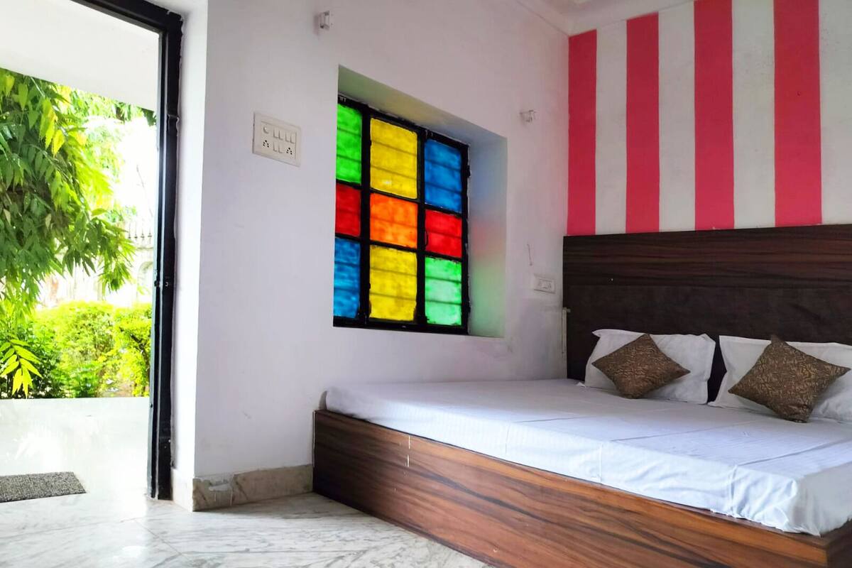 A bedroom with a bed, a window with colorful stained glass, and a view of greenery outside.