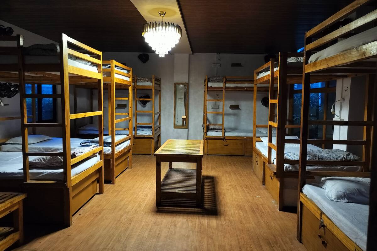 A dormitory room with bunk beds, a wooden table, and a chandelier.