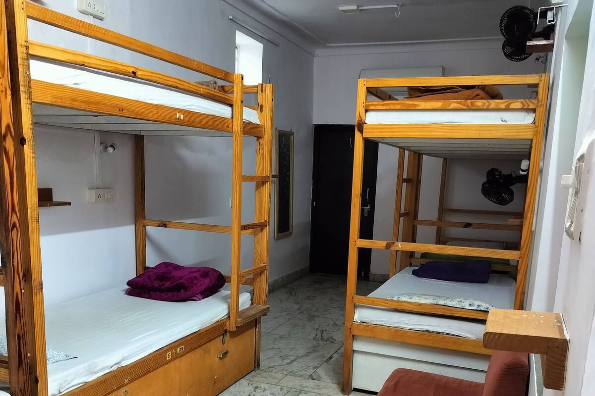 A dormitory room with two bunk beds, a small wooden bench, and a tiled floor.