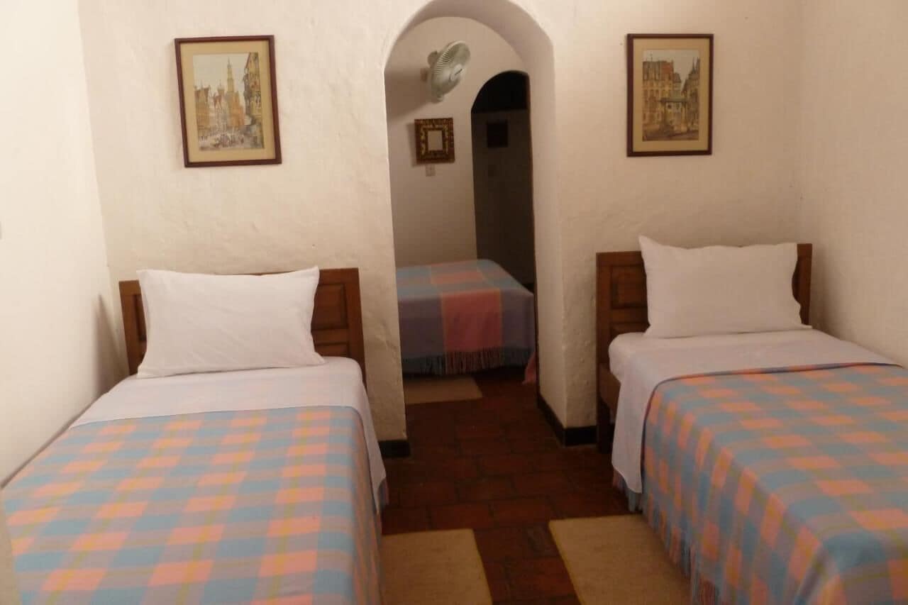 Una habitación con dos camas, cada una con colcha a cuadros, una mesita y un cuadro en la pared.