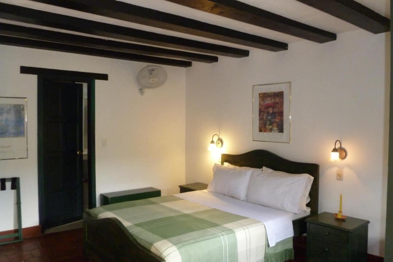 Un dormitorio con cama, mesitas de noche, una puerta y un aplique en la pared.