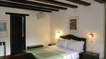 Un dormitorio con cama, mesitas de noche, una puerta y un aplique en la pared.