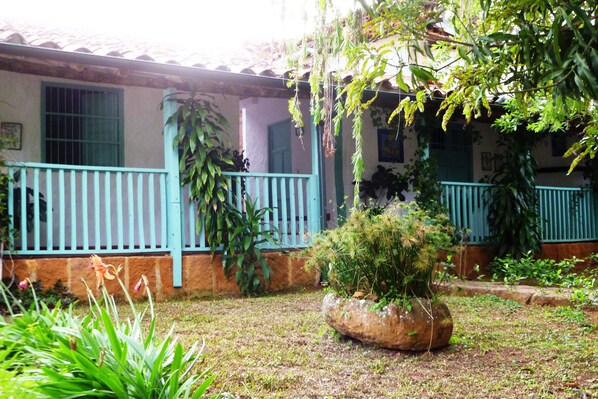 Un patio con un muro de piedra, una jardinera grande de roca y un edificio con techo de tejas y barandillas azules.