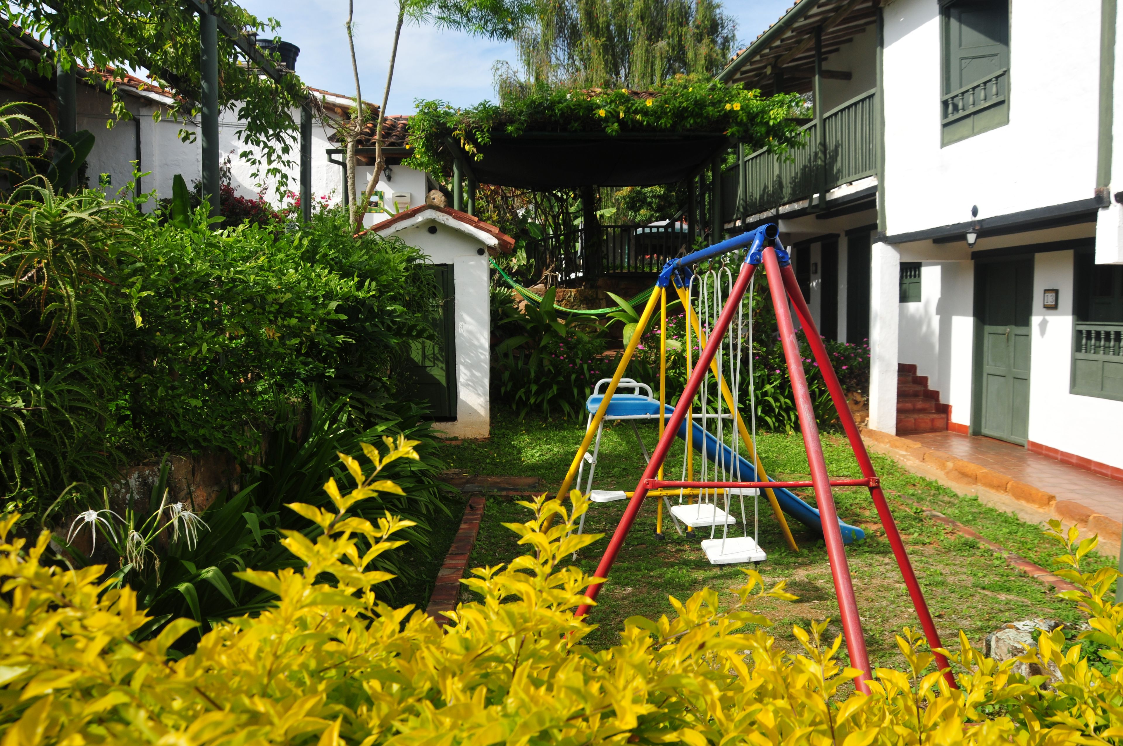 Un jardín con un columpio, un edificio blanco pequeño y una casa con balcón.