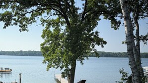 A wooden deck leading to a dock by a lake, surrounded by grass and trees.