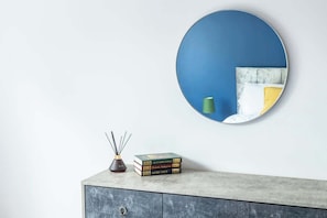 A round mirror on a wall, a small cabinet with books, and a candle holder. - Big & Beautiful Home | Free Driveway Parking (Nottingham)