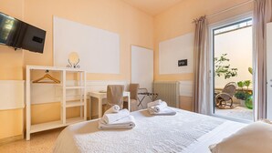A hotel room with a bed, a TV, a desk, a chair, a hanging towel rack, and a view of the outside. - Holiday Studio at Dimora Le Tre Muse Charming Guesthouse in Lecce (Lecce)