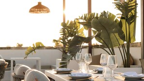A dining table set with plates, glasses, and napkins, surrounded by chairs and large tropical plants. - Holiday Studio at Dimora Le Tre Muse Charming Guesthouse in Lecce (Lecce)