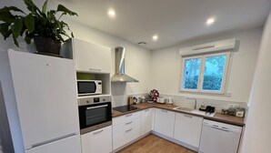 A modern kitchen with white cabinetry, a built-in oven, microwave, and dishwasher. There is a window with a view of trees outside. - La Pascaline, Appt 47m² 1er Étage Avec Belle vue (Saint-Clément-de-Rivière)