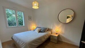 A bedroom with a bed, bedside lamps, a round mirror, and a window with a view of trees. - La Pascaline, Appt 47m² 1er Étage Avec Belle vue (Saint-Clément-de-Rivière)
