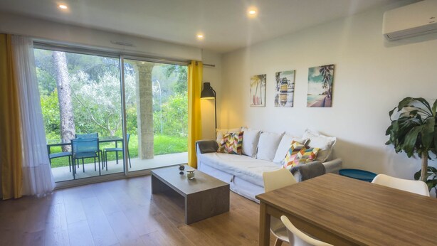 A modern living room with a sofa, a dining table, and a coffee table. There is a large window with curtains, a lamp, and artwork on the wall.