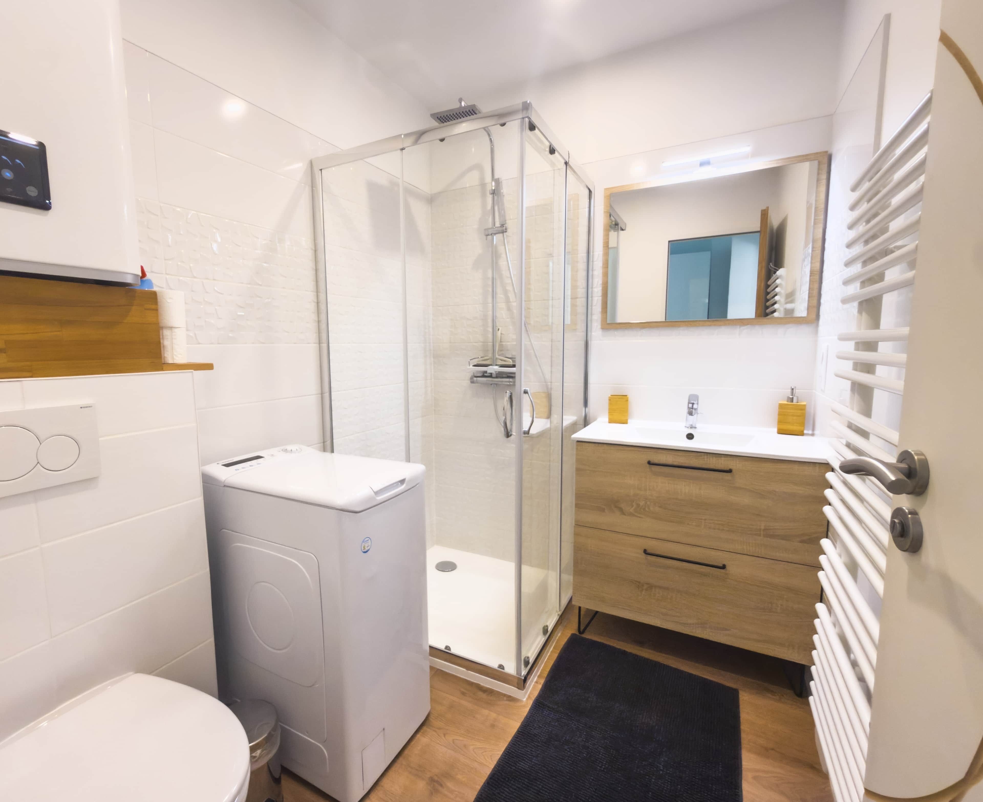 Une salle de bain moderne avec une douche à parois de verre, des toilettes blanches, un lave-linge, un meuble-lavabo en bois avec un miroir et un radiateur.