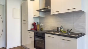 A modern kitchen with white cabinets, a black countertop, a built-in oven, a stainless steel sink, and a red kettle.