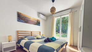 A bedroom with a wooden bed, a nightstand, a lamp, a painting, and a large window with curtains.