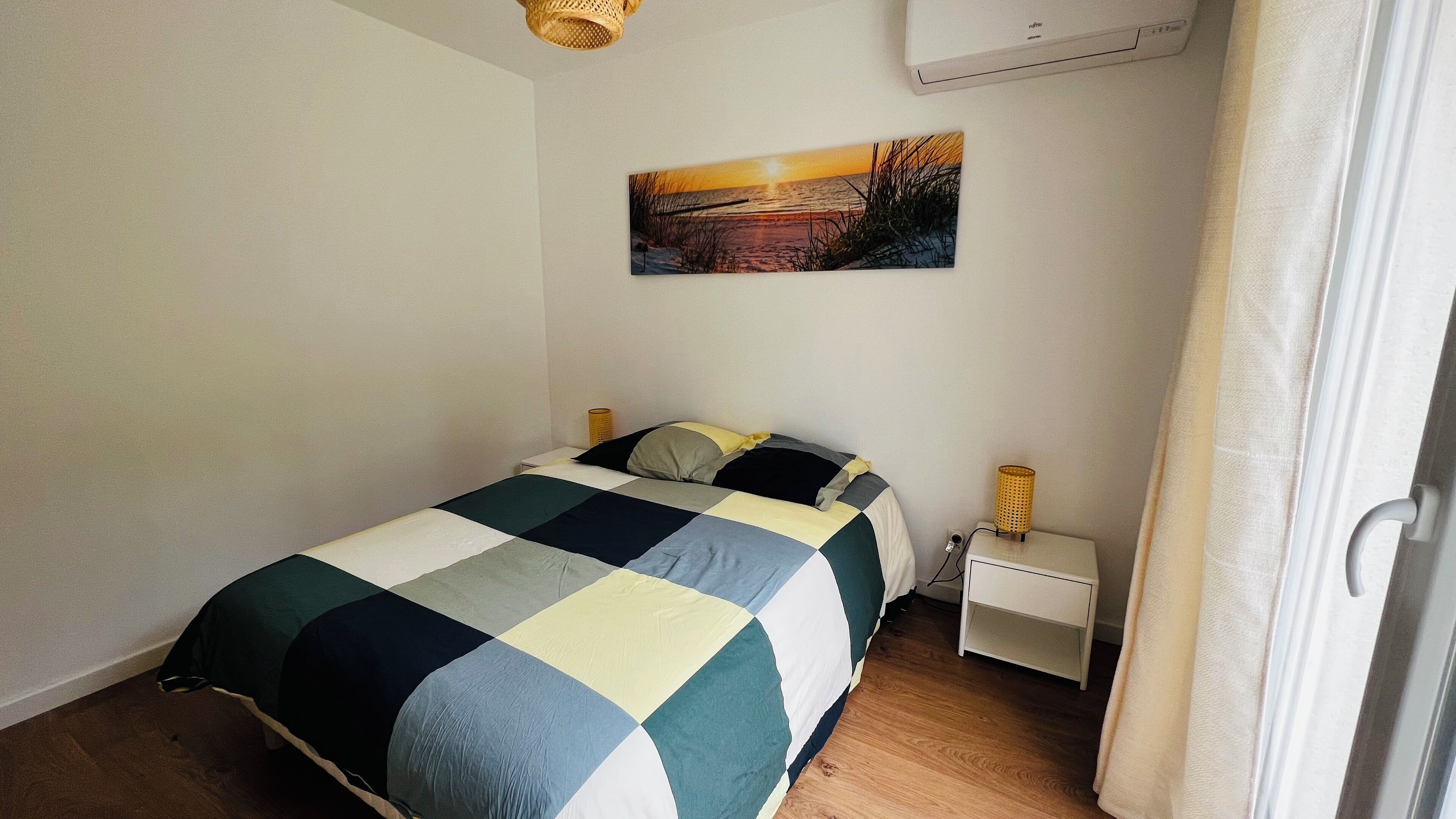 Une chambre à coucher bien rangée, avec un lit, des tables de chevet, un climatiseur fixé au mur et un tableau.