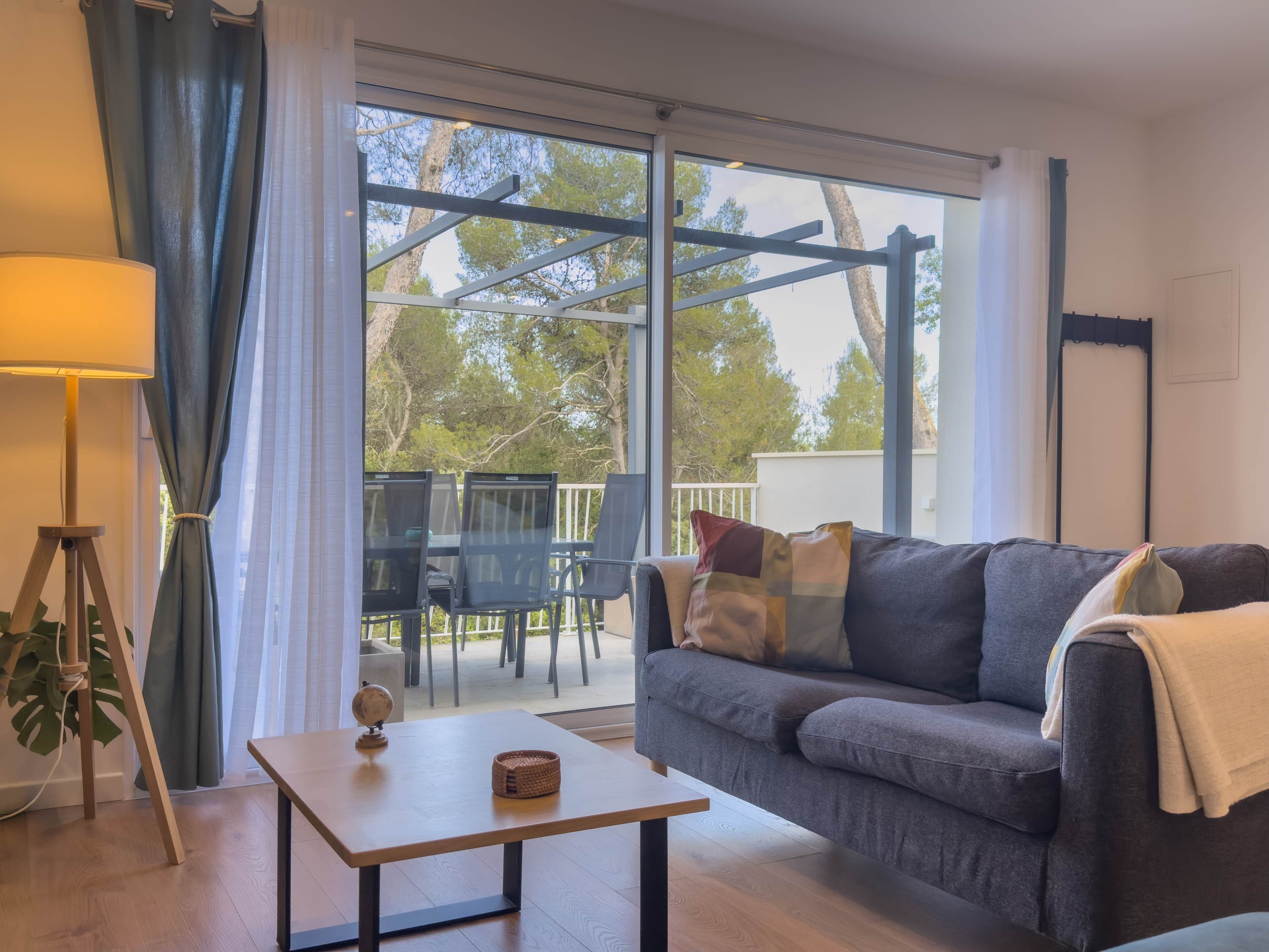 A living room with a sofa, a table, a lamp, and a view through a large window.