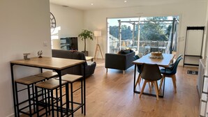 A modern living space with a dining area, a sofa, a TV, and a balcony with a view of trees. - To complete (Saint-Clément-de-Rivière)