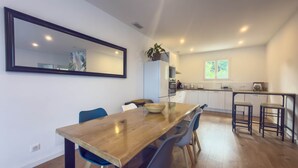 A modern kitchen with white cabinets, a wooden dining table with blue chairs, and a large mirror on the wall. - To complete (Saint-Clément-de-Rivière)