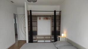 A bedroom with a bed, a bedside table with a lamp, a wardrobe with multiple shelves, and a door leading to another room. - To complete (Saint-Clément-de-Rivière)