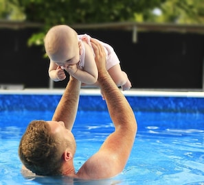 Een man houdt een baby boven een zwembad.