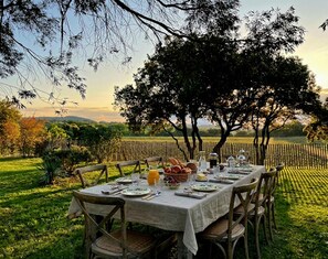 Ein Tisch mit Stühlen im Freien, umgeben von Bäumen und einem Feld im Hintergrund.