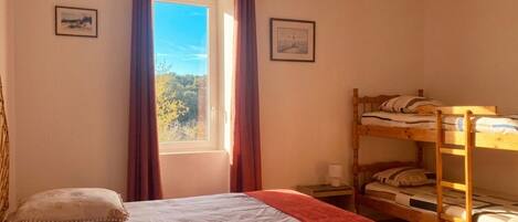 A bedroom with a single bed, a bunk bed, a window with curtains, and a hanging light fixture.