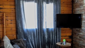 A cozy cabin interior with a wooden ceiling, a sofa, a television mounted on the wall, and a small round table with a remote control. - Gothes Chalet Javier!! (Ponte de Vagos)
