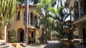 Une cour avec une fontaine, des palmiers et un bâtiment doté d’arcades et de balcons.